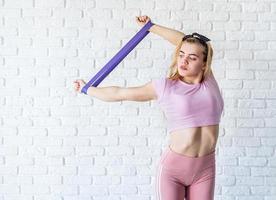 Athletic woman doing exercises using a resistance band at home at white brick wall background photo