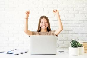 Female teenager learning from home sitting at the desk with arms raised photo