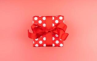 Single red gift box with red ribbon on pink background top view photo