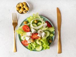 Ensalada griega con queso feta, verduras frescas y aceitunas sobre fondo blanco rústico vista superior