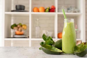 Avocado and spinach smoothie in glass bottle front view on home kitchen background photo