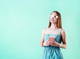 Emocionada chica adolescente con gafas 3d comiendo palomitas de maíz aislado sobre fondo azul. foto
