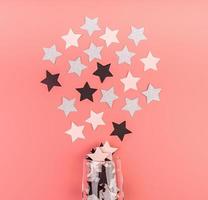 star shaped confetti pouring out of the glass on pink background flat lay top view photo