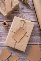 Gift boxes wrapped in craft paper with tags and labels on wooden background top view flat lay photo