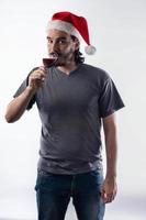Young Latino man in Santa Claus hat, drinking a glass of wine and looking at camera. isolated on White background photo