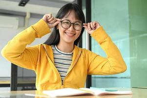 estudiante asiática con gafas y sonrió a la cámara. ella está leyendo libros de preparación para exámenes. foto
