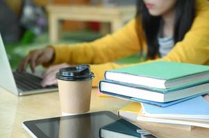tazas de café y un cuaderno sobre la mesa con una estudiante adolescente están usando la computadora portátil en la parte posterior.