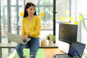 Asian female programmer for yellow shirt sit on the shelf and place laptop on leg.She stared at computer screen on the table and pondered. photo