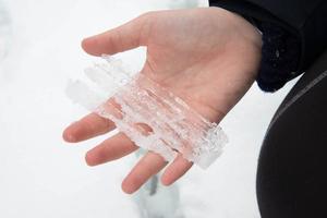 Piece of ice on a young caucasic woman hand. Snowed landscape around photo