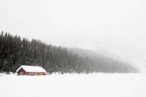 Beautiful winter landscape with snow. A wooden house close to a forest during a heavy snow storm. Banff National Park, Canada. photo