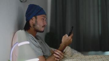 Hombre asiático usando un teléfono móvil mientras está acostado en la cama en su casa.