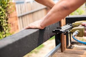 Hand man carpenter using air nail gun to complete wood table in garden photo