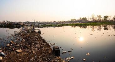 Polluted water and mountain large garbage pile and pollution at the sun is setting in the background photo