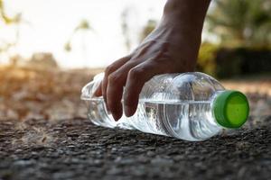 Close up Hand picking up clear plastic bottle water drink with a green cap on the road in the park at blurred background, Trash that is left outside the bin photo
