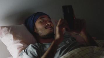 aziatische man die een mobiele telefoon gebruikt terwijl hij 's avonds laat thuis in bed ligt.