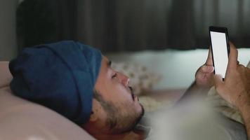 aziatische man die een mobiele telefoon gebruikt terwijl hij 's avonds laat thuis in bed ligt.