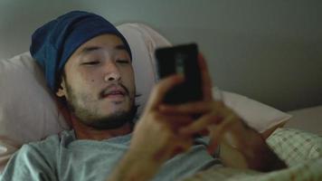 Hombre asiático que usa un teléfono móvil mientras está acostado en la cama en su casa a altas horas de la noche. video