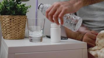 Hombre asiático vertiendo agua en el vaso mientras está en el dormitorio en casa. video