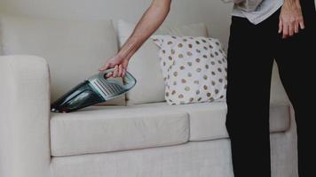 Hombre asiático limpiando el sofá con una aspiradora en la sala de estar de casa. video