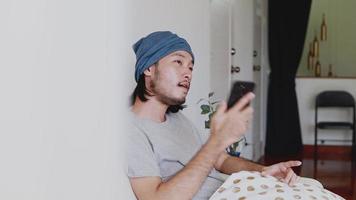 empresário asiático falando ao telefone enquanto está sentado em um sofá na sala de estar em casa. video