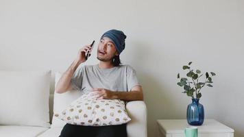 hombre de negocios hablando por teléfono y tomando café mientras está sentado en un sofá en la sala de estar de su casa. video