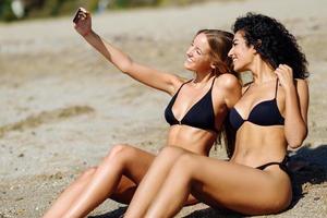 Dos mujeres tomando fotografías selfie con smartphone en la playa. foto