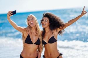 Two women taking selfie photograph with smartphone in the beach photo