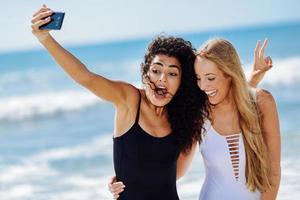 Two women taking selfie photograph with smartphone in the beach photo