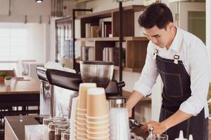 young asian man using coffee maker machine to brew hot expresso. barista and coffee cafe concept photo