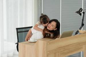 young asian mother and her kid using computer to video call online with father at home. distance communitacion concept photo