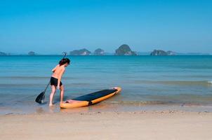 Joven mujer deportiva jugando stand-up paddle board en el mar azul en un día soleado de vacaciones de verano