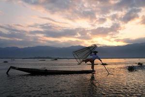 Silueta de pescador local usando coop para pescar en el lago Inle al amanecer. foto
