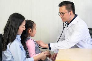 asian doctor let the young girl use stethoscope to listen to his heart and lung. healthcare and pediatrician concept photo