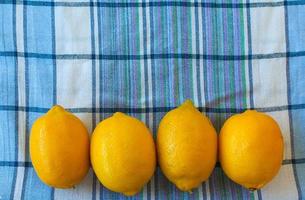 Still life of big ripe yellow lemons lying on checkered towel with glass of lemon juice on windowsill in sunlit room. photo