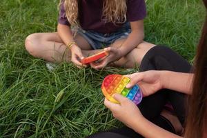 Girls play colorful silicone touch popular pop-it toy outdoors on green grass photo