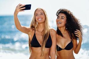 Two women taking selfie photograph with smartphone in the beach photo