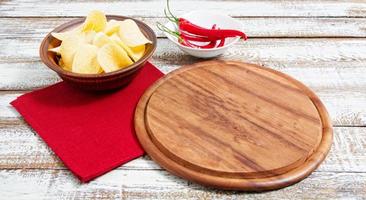 spicy red chilli potato chips and empty board on a wooden table photo