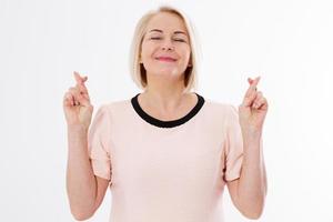 Portrait of superstitious midle-aged female with crossed fingers, Mature businesswoman with closed eyes holding fingers crossed isolated on white background, white lady keeping her fingers crossed photo