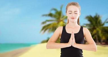 Woman with closed eyes in namaste pose on tropical beach ocean sea background - summer yoga concept photo