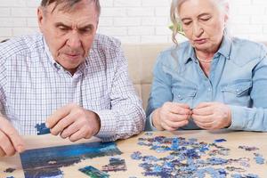 pareja de ancianos recogiendo rompecabezas en casa, pareja de ancianos jugar rompecabezas foto