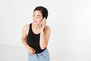 Sonriente mujer japonesa asiática mantenga blanco smartphone o teléfono móvil aislado sobre fondo blanco textura concepto publicitario. expresión facial positiva emoción humana. copie el espacio. foto