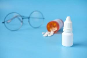 close up of eye drop bottle and eyeglass on blue background , photo