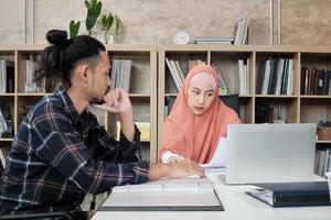 dos jóvenes colegas de la startup que son personas islámicas hablan sobre proyectos financieros que trabajan en un negocio de comercio electrónico con una sonrisa. Utilice la computadora portátil para comunicarse en línea a través de Internet en una oficina pequeña. foto