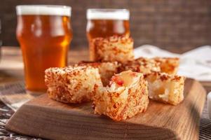 Tapioca dice with pepper jelly and glasses of beer on a wooden cutting board - Closeup. photo