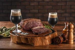Grilled cap rump steak on wooden cutting board with two sweaty tulipa glasses of dark draft beer. photo
