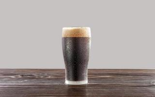 Isolated sweaty glass of refreshing dark draft beer with white background. photo