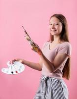 woman artist with a color palette and paintbrushes isolated on pink background photo