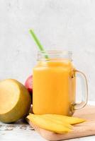 mango smoothie in a mason jar decorated with slices of mango front view on wooden background photo