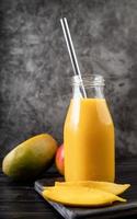 fresh mango shake in a glass with a metal drinking straw decorated with slices of mango front view on dark background photo