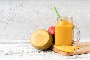 mango smoothie in a mason jar decorated with slices of mango front view on wooden background